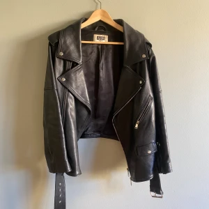 Skinnjacka i biker-modell  - Ballaste vårjackan!  Skinnjacka från Weekday i storlek XS, oversize så passar mig som vanligtvis har S.   Använt skick. Skinnet är fint, tyvärr har en av hällorna till bältet gått upp men borde inte vara svårt att fixa. 
