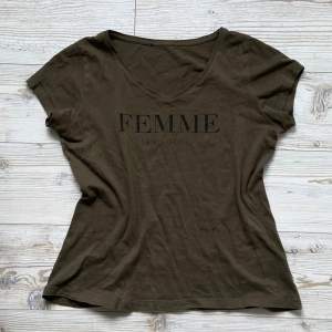 Superfin khakigrön t-shirt med v-ringning och texten ”Femme en Vogue” 🖤 Den har ett litet hål (se bild 2). Taggarna är bortklippta så vet inte storlek men skulle säga S/M!