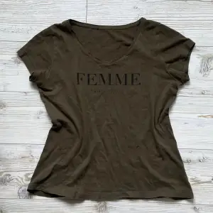 Superfin khakigrön t-shirt med v-ringning och texten ”Femme en Vogue” 🖤 Den har ett litet hål (se bild 2). Taggarna är bortklippta så vet inte storlek men skulle säga S/M!