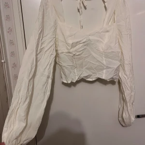 Blus / magtröja - Skrynklig då den legat i en väska med andra kläder. Långärmad blus som är som en magtröja. Ärmarna är oversize modell. Bilderna är tagna med och utan blixt. Man ser lite igenom vid magen av tröjan men inte vid bysten när man tar bilder nära med blixt