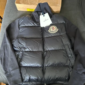 Moncler cardigan - Ny med lappar. Mörkblå Moncler cardigan stl M inköpt på wakaku. Dun fram och ärmar och bakstycke i collegematerial. Tyvärr för stor och försent att lämna tillbaka. Finns att köpa på Moncler.com för 10.600 sek. 