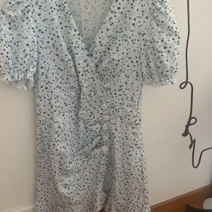 Klänning - Jätte somrig klänning. Vit med blåa blommor. Sitter tajtare vid magen och går ut lite där nere. Nytt skick