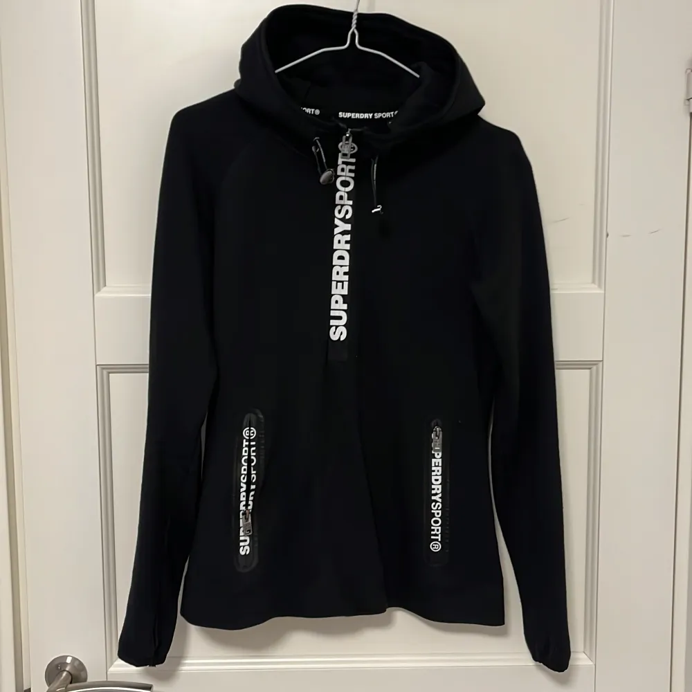 Väldigt fin hoodie från Superdry Sport. Både sportig och snygg till vardagligt bruk. I bomullsmaterial, eller samma material som vanliga hoodies. Fräcka detaöjer med tryckt text på blixtlåsen och bak nertill. Storlek S, i fint skick!!. Hoodies.