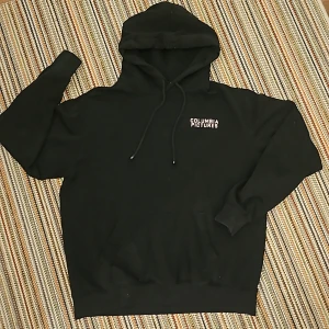 Hoodie  - Svart hoddie med end logga på bröstet och en bild på ryggen