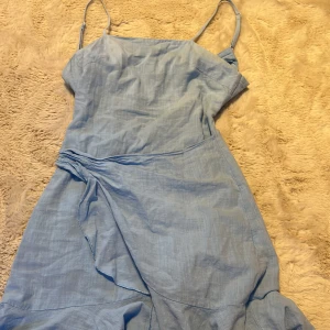 Blå omlott klänning - Använd 1 gång, inga fläckar/skador. Väldigt fin, man ska knyta vid ryggen och där framme. Dragkedja där bak. Ännu finare i verkligeheten.