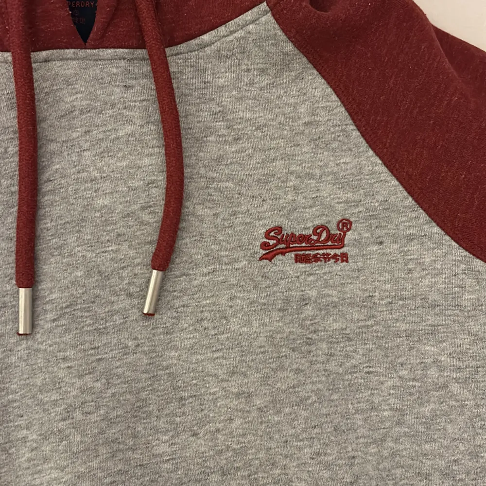 Röd/grå hoodie från Superdry i storlek S. Köpte den för ca 1 år sen men har knappt använt den. Säljer nu eftersom den inte riktigt passar mig längre.. Hoodies.
