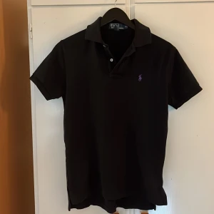 Ralph lauren piké  - En svart polo ralph lauren piké med lila logga äkta använd men inte sliten har ingen användning för den längre. För mer info kom PM.