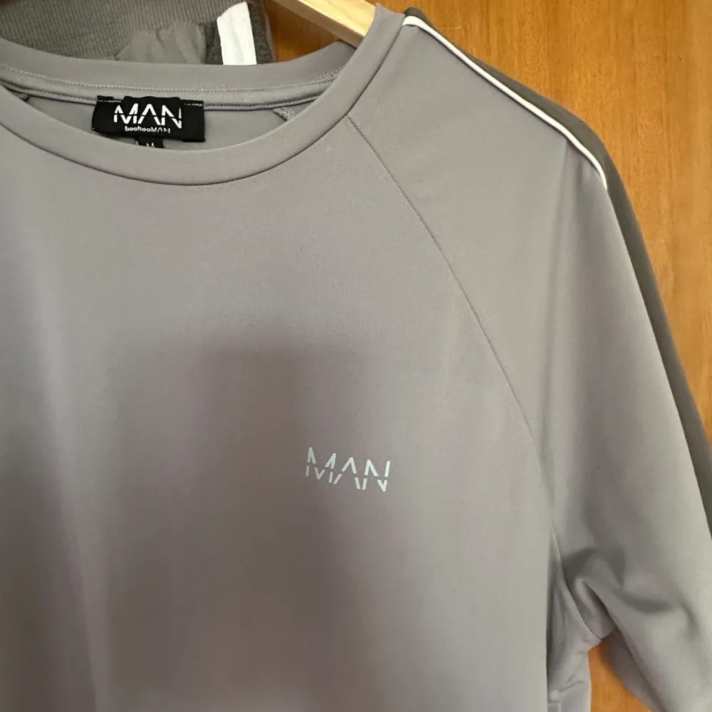Ett par gråa joggingbyxor från MAN, samt en T-shirt från samma märke. Storlek L i byxorna och M i tröjan. Hoodies.