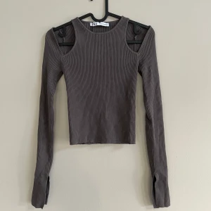 Ribbad topp från Zara  - Grå/brun topp från Zara i nyskick! Denna fina topp är ribbad och har snygga detaljer som cut outs och slitsar. Toppen är köpt för 259kr och har aldrig använts. Det är bara att skriva om du vill ha fler bilder eller har några funderingar!😊