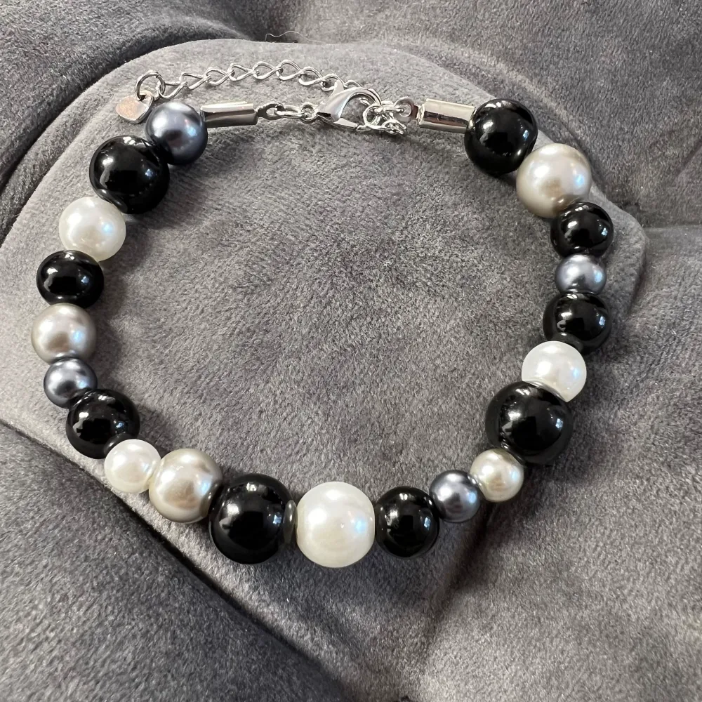 Handgjort pärlarmband med svarta, gråa och vita pärlor och silverfärgat spänne. Justerbar passform mellan 20-25 cm.. Accessoarer.
