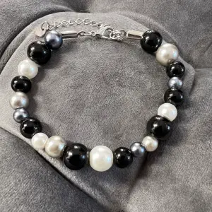 Handgjort pärlarmband med svarta, gråa och vita pärlor och silverfärgat spänne. Justerbar passform mellan 20-25 cm.