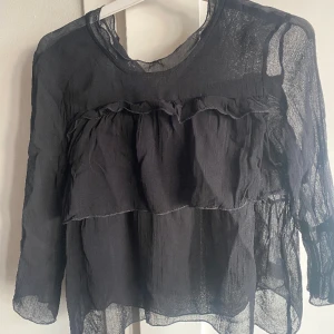 Svart volangtopp neo noir  - Svart tunn volangtopp från Neo Noir. Knappen bak har lossnat och behöver sys fast. Annars i fint skick. Storlek S. Armarna är 3/4 längd. Rök- & djurfritt hem. 