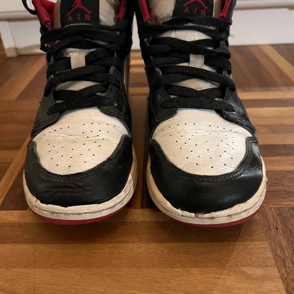 Air Jordan 1 Mid i svart, vitt och rött. Bra skick med något slitage på sulan framme vid tårna. Storlek: 36. Skor.