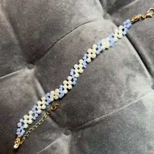 Handgjort pärlarmband med ränder i vitt och ljusblått med guldigt spänne. Justerbar passform mellan 19-24 cm.