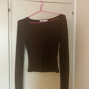 Brun långärmad tunn topp med urringning  - Varan är långärmad och i tunnt material. Den är urringad och går att användas till vardag såväl som vid speciella tillfällen. Den är lagom i storleken och varken jättelång eller magtröja. Har används fåtal gånger så är i mycket bra skick.
