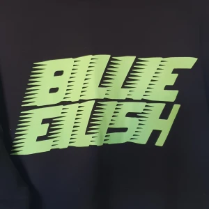 Tröja Billie Eilish - Svart tröja. Troligtvis från H&M. Lapparna är tyvärr bortklippta. Gissar att det är en storlek L. Använd 1 gång. Ljusgrön text på framsidan av tröjan. Mjuk, flossad insida. 
