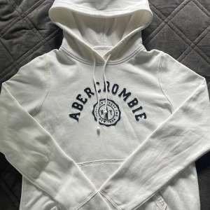 Hoodie från Abercrombie & Fitch  - En vit hoodie med marinblått broderi på framsidan från Abercrombie & Fitch i storlek M. Den är i bra skick, men har dock en mycket liten fläck längst ner på höger ärm som (Se bild 5) troligtvis går bort i tvätten. 😊