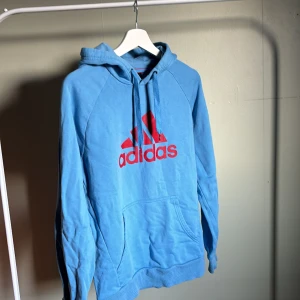 Blå/röd adidas hoodie - Blå hoodie med röd text från adidas i stl M. Passar S-M. I bra skick men lite smått nopprig därav lägre pris. 