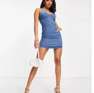 Jeansklänning - En snygg denimklänning med halterneck och urringning. Dragkedja finns i ryggen för att enkelt få på och av klänningen. Strl 34  Aldrig använd 