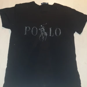 Polo t-shirt - En svart polo t-shirt. Den har fått 2 blek fläckar en där bakom en där framme 