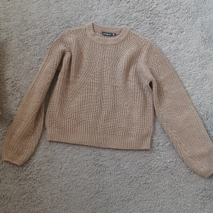 Beige stickad tröja från XOXO Friends - En beige stickad tröja från XOXO Friends. Tröjan har ett enkelt mönster och är tillverkad av 100% akryl. Den har långa ärmar och ribbstickade muddar vid ärmslut och nederkant.