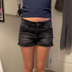 Svarta jeansshorts - Ett par svarta jeansshorts med upprullade ben. Shortsen har en knapp och dragkedja framtill samt flera fickor både fram och bak.
