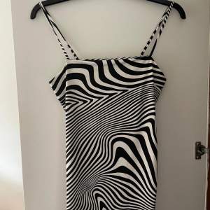 En svartvit klänning med zebrastilsmönster. Klänningen har smala axelband och en åtsittande passform. Den har en knytning på sidan för justering av längden. Köpt på H&M och endast använd en gång. 🦓 🤍✨
