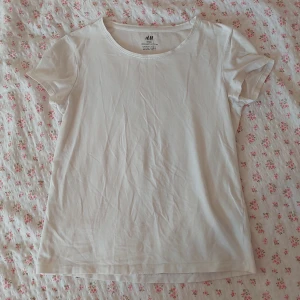 Vit t-shirt från H&M - En enkel och bekväm vit t-shirt från H&M med korta ärmar och rund halsringning. Perfekt för vardagsbruk. Strl 146/152 Katt finns i huset.