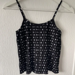 Kort svart topp - Söt svart topp med vita prickar. Aldrig använd då den är för liten. Troligt vis köpt på Gekås. Inte stretchig. I mycket bra skick. 