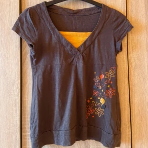 Tröja/T-shirt - Mörkbrun tröja med orange bit vid bröstet och blommiga detaljer på sidan. Står inget märke på den men trycker in Zara.✨ Passar S-M. Nyskick