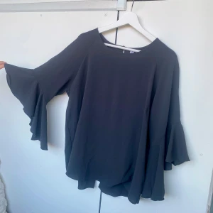 Grå blus  - Mörkgrå blus i storlek L. Fina volangärmar och delvis öppen i ryggen(se bilder) 
