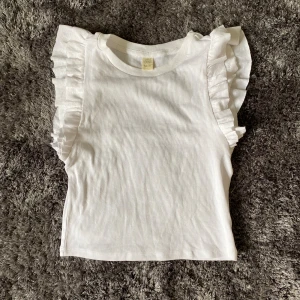 Ribbad volang topp - Super söt ribbad vit topp med volanger på axlarna. Strl 146/152 men passar mig som har xs-m. Endast testad på en gång! Priset är + frakt. Använd inte köp nu utan kontakta mig privat vid intresse!