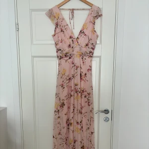 Vacker festklänning öppen rygg, rosa, blommig - Festklänning storlek 36. Öppen rygg med knytdetalj, lång böljande kjol, underklänning så du genomskinlig. Mycket vacker. Använd på ett bröllop, tvättad en gång efter det. 