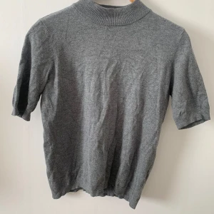 Stockh LM grå tröja, storlek S - Snygg grå tröja med hög hals och korta ärmar. Tröjan är i en mjuk och skön kvalitet.  Skick: Mycket bra Axelbredd: 35cm Längd: 56cm