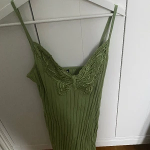Grön klänning med säkring  - En jättefin grön klänning med en fjäril vid bröstet som smälter in väl. Väldigt skönt matrieal och går lite ovanför knäna formar kroppen väldigt bra. 