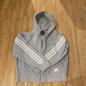 Adidas sip hoodie - En grå adidas sip hoodie. Har en liten fläck där fram ( se bild 3 ) men den syns knappt. Är i storlek 160 och är lite liten för mig som bär S.
