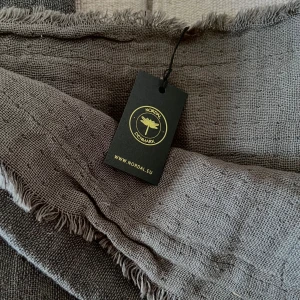 Nordal yoga sjal/filt bomull mörkgrå - Ny, oanvänd yoga sjal/filt från Nordal. Gjord av naturmaterial i en blandning av bomull och linne (75% bomull, 25% linne). 160x140 cm. Används för mysiga stunder och när det är svalt, till före/efter t.ex yoga eller under t.ex meditation. Mörkgrå.