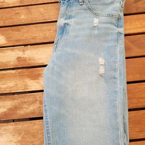 Ljusblå jeans - Ett par  ljusblå jeans med slitna detaljer och fransig nederkant. Jeansen har en knapp och dragkedja framtill samt fickor. Använda få tal gånger.