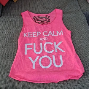 Rosa ärmlös topp med text - En rosa ärmlös topp med texten 'KEEP CALM AND FUCK YOU' i vitt på framsidan. Toppen har en öppen rygg med horisontella remsor som skapar ett unikt mönster.