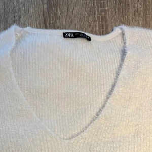 Vit stickad tröja från Zara - En mjuk och fin vit stickad tröja från Zara med v-ringning. Tröjan har långa ärmar och en enkel design som passar bra till både vardag och fest.