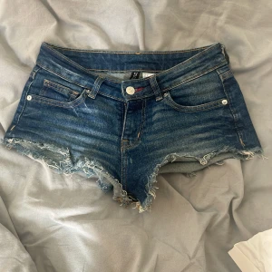 Blå jeansshorts från H&M - Ett par blå jeansshorts från H&M med råa kanter och slitna detaljer. Shortsen har fem fickor och en knappgylf. kom gärna med prisförslag 