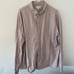 Cos skjorta  - Säljer en snygg skjorta från Cos i XL. Färgen är grårosa och har fadeats in jättefint. Bra skick, inte speciellt använd.