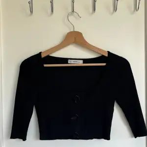En svart croppad tröja som är i ribbat material med knappar på framsidan ( går inte att knäppa upp ). Knappt använd! 