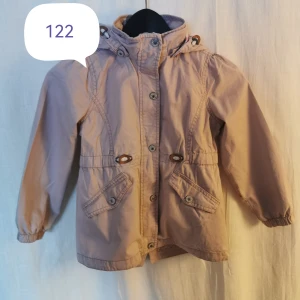 Barn vårjacka 128 - Avtagbar luva Tunnt fodrad Ställbar midja *liten fläck på vänster underarmens insida, syns lite på bilden framifrån.   Försöker syna och få med skavanker, friskriver mig från att missat någon detalj