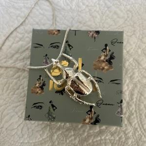 Ioaku halsband! - Säljer mitt superfina ”Beetle Mini” halsband från Ioaku i silver som knappt har använts och är i superfint skick. Köptes för 600kr och säljer för 400kr då även boxen samt en längre kedja till halsbandet tillkommer. 