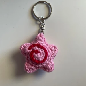 Stjärnnyckelring med swirldetalj - Handvirkad nyckelring med gullig swirl detalj<3 Kan göras i flera färger, skriv privat! Gjord av 100% bomullsgarn. Mått: 4,5 x 4,5 cm