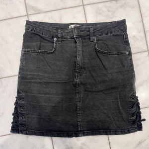 Svart jeanskjol - Cool svart jeanskjol med snörade sidor. Strlk 38 men passar mig som brukar ha 34/36. Skriv för fler bilder