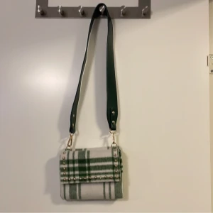 Hvisk grön väska - Hvisk grön väska med guldiga detaljer. Säljer pga den aldrig kommer till användning. Väskan är gjort i tyg. Och inne i väskan är det ett stort fack på båda sidorna!