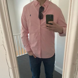 Ralph Lauren Skjorta - Tja, säljer min rosa Ralph Lauren skjorta! Skjortan är i storlek L och modellen på bilden är ca 190cm och väger 80kg. Den är nästan helt ny och man ser inga tecken på att den är använd. Den klippta taggen finns och skickas med. Skriv för mer information!