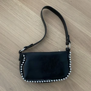 Liten axelväska - Liten axelväska i läderimitation med pärlor på. Oanvänd och i nyskick. 100kr